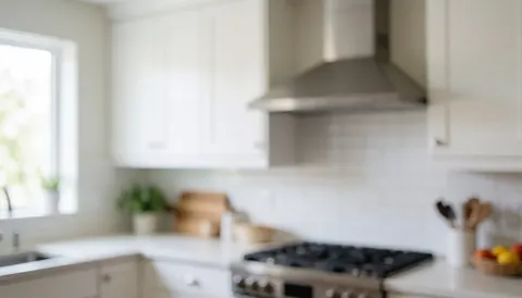 Modern kitchen featuring a stainless steel range hood, white cabinets, and natural light, suitable as a professional text background.