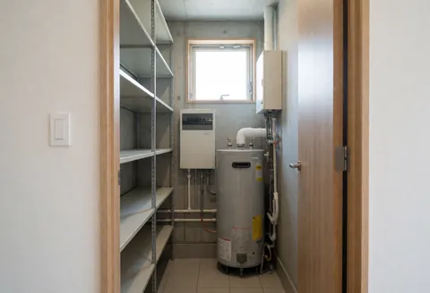 Utility room featuring a boiler, metal shelves, electrical panel, and window with natural light