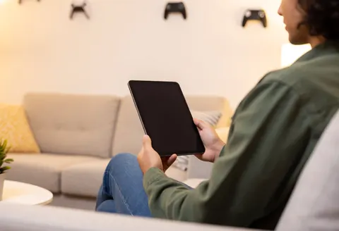 Person sitting on a sofa using a tablet in a warm, professional waiting room with gaming decor on the walls.