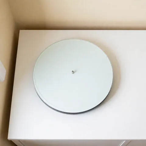 Clean white microwave turntable plate resting on a white surface with bright, even lighting and beige walls in the background.