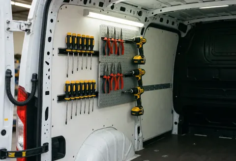 White van interior with screwdrivers, pliers, and drills on the dashboard and magnetic mounts under fluorescent lighting, ideal for installation services.