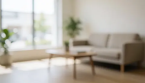 Modern waiting room background featuring a beige sofa, wooden coffee table, and plants with soft natural lighting, ideal for advertising text overlay.