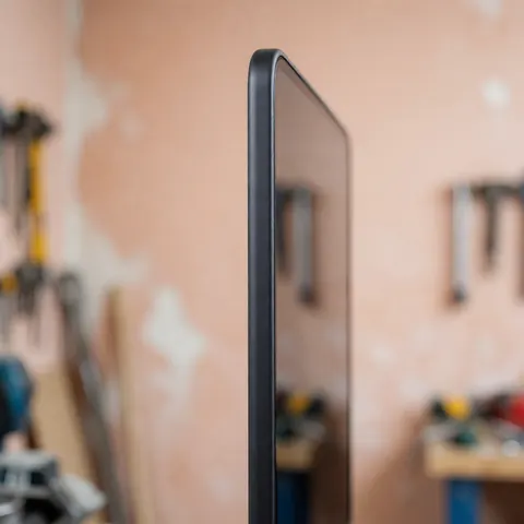 New cell phone screen with rounded black border shown in side view at workshop with blurred tools on terracotta background