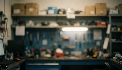 Out of focus background of a computer repair workshop featuring shelves, tools, and a computer with warm lighting and blue and grey tones