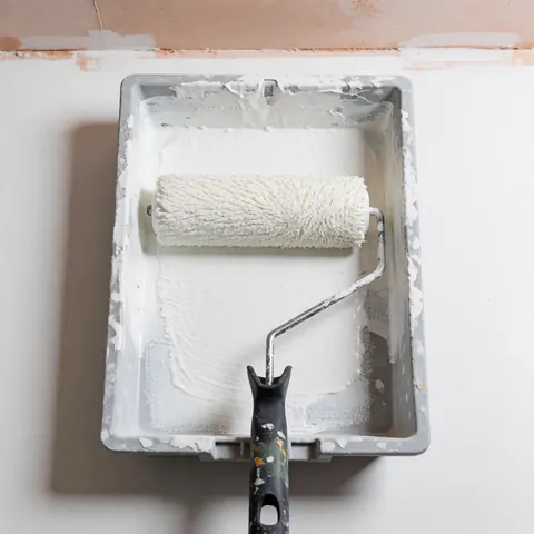 A white paint roller resting in a gray plastic tray, prepared for wall repair and painting tasks.