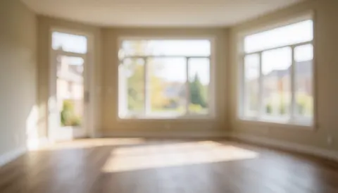 Empty living room with wooden flooring, large windows, and soft natural light, ideal for text overlays and flooring installation projects