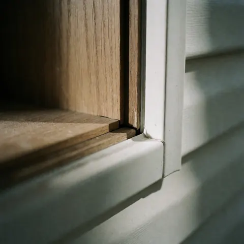 Close-up view of the junction between a wooden frame and a white vinyl profile, highlighting the natural texture and smooth finish quality.