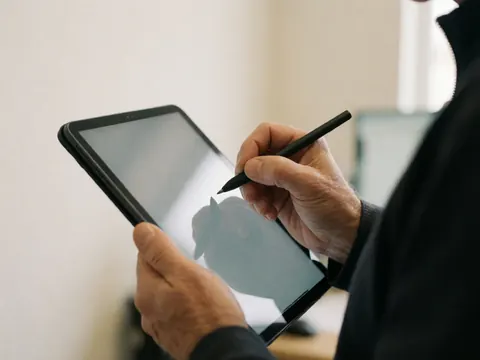 Close-up of an adult hand using a stylus to sign on a digital tablet in an office setting
