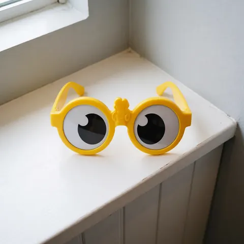 Yellow sunglasses with large lenses resting on a white shelf near a window, suitable for amusement park souvenirs.