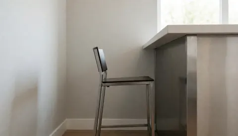 Metal bar stool with black seat beside polished metal counter in modern clean space with gray walls