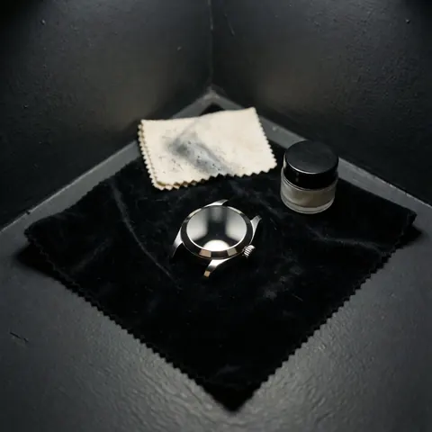 Polished watch case with reflections on black cloth, next to polishing cloth and compound jar in gray corner