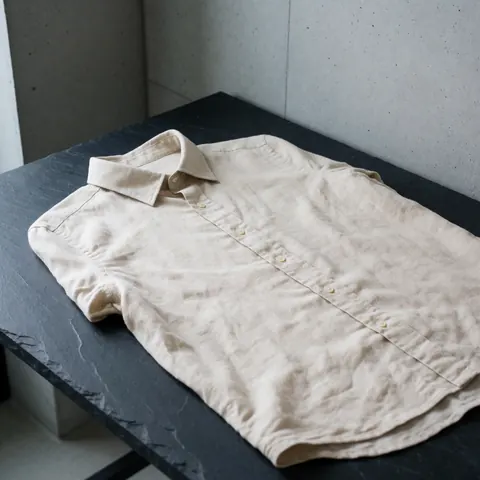 Beige linen shirt with buttons on a dark stone table with concrete walls and natural light