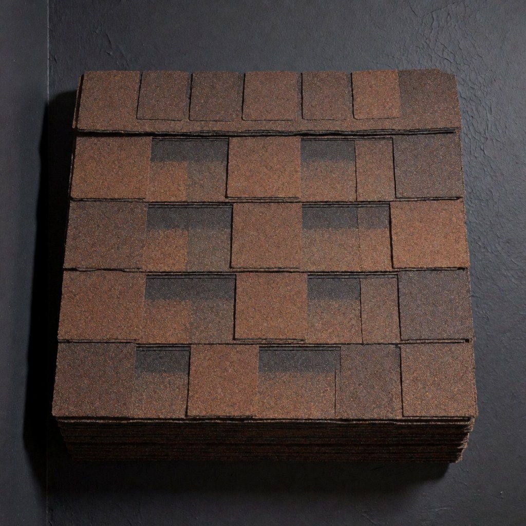 Stacked brown asphalt shingles arranged in a grid pattern, showing granular texture and overlap design on a charcoal gray background.