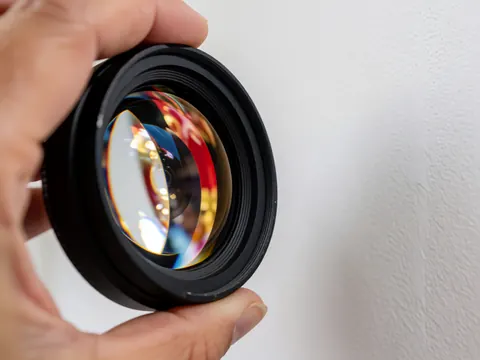 Close-up of a camera lens held by a hand, reflecting vibrant parade colors against a white background with bright lighting