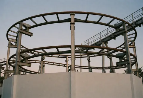 Curved steel roller coaster structure with walkways against a twilight sky, suitable for theme parks and promotional use.