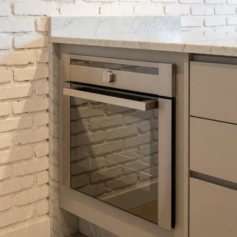 Built-in stainless steel oven set in a kitchen island with white marble countertop and white painted brick wall reflecting ambient light