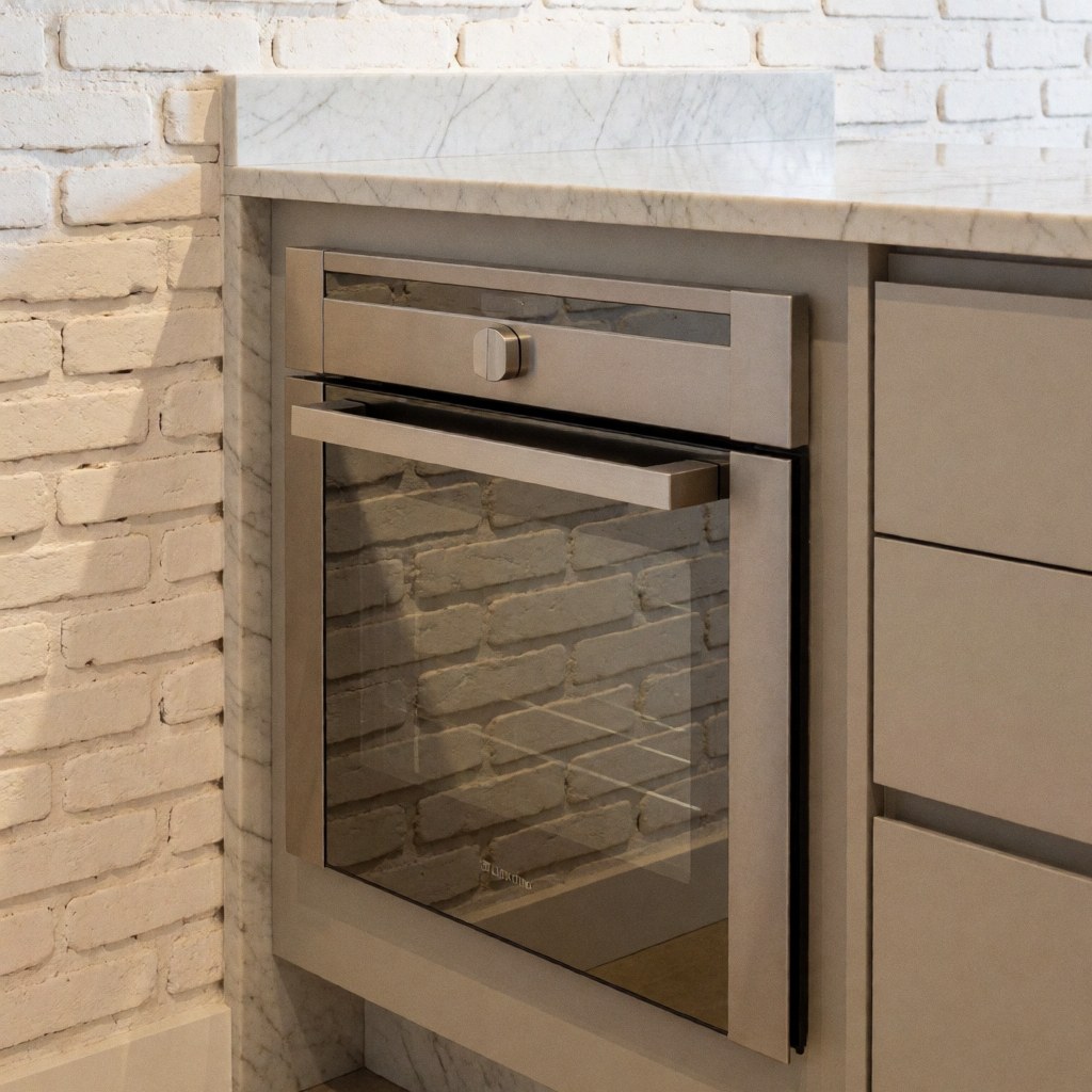 Built-in stainless steel oven set in a kitchen island with white marble countertop and white painted brick wall reflecting ambient light