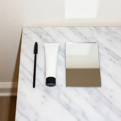Eyebrow lamination kit with brush, gel tube, and small mirror on white marble for beauty services