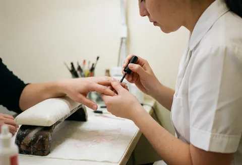 A manicurist carefully applies black nail polish to a client's nails during a professional salon service.