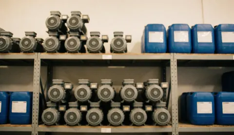 Industrial warehouse background with shelves full of gray filtration pumps and blue containers, ideal for business text.