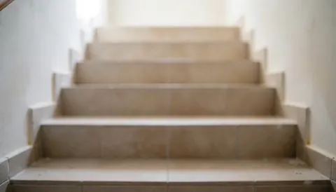 Interior view of beige tiled stairs with blurred grout lines and white walls, serving as a professional background for commercial text.