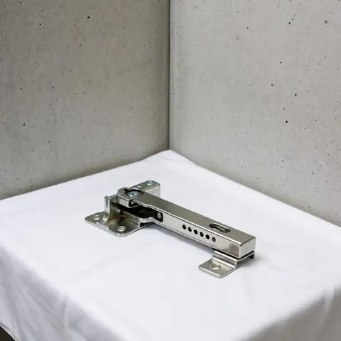 Close-up of a new, shiny metal refrigerator hinge resting on a white fabric surface with a polished concrete background and soft professional lighting