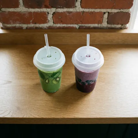 Two fresh smoothies, one green with kiwi and one purple with fruit, in glasses on a light wooden table with a red brick wall.