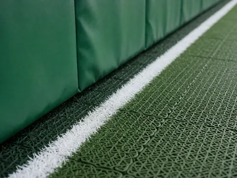 Close-up detail of the corner where a green stitched wall meets a synthetic turf floor with white marked lines, suitable for a sports club.