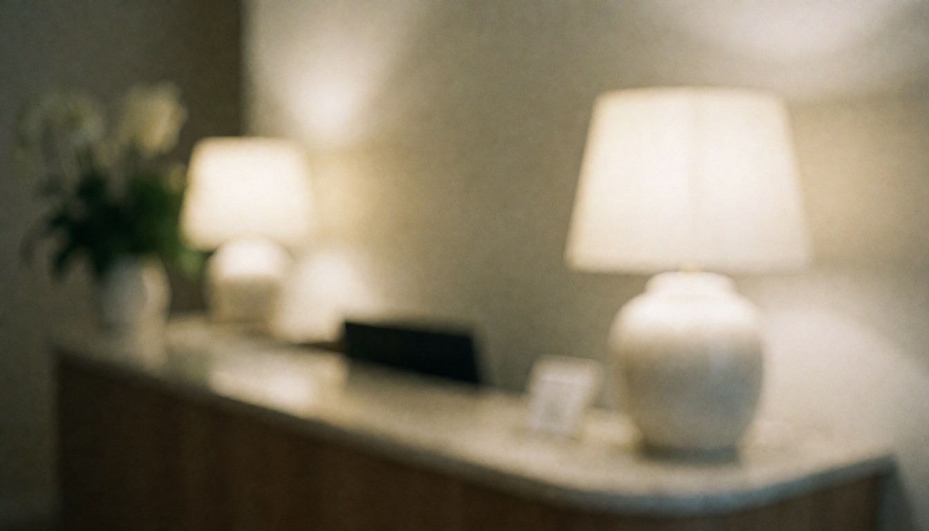 Soft focus background of a professional reception area featuring two white table lamps, a green plant, and a wooden counter with warm lighting.