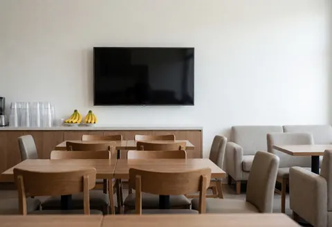 Empty waiting room featuring wooden tables, comfortable chairs, a television, and fruit, ideal for a sports club interior.