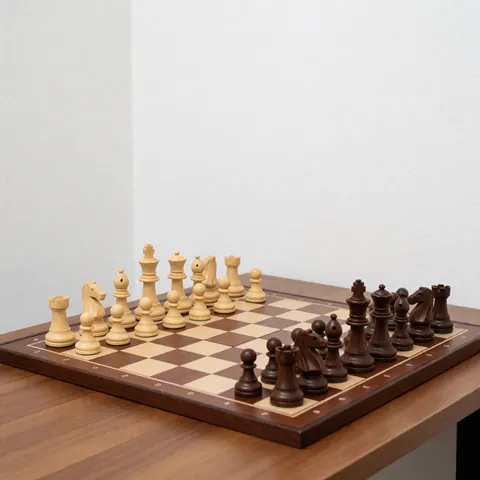 Wooden chessboard with light and dark pieces set up for a game on a wooden table against white walls with bright professional lighting