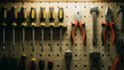 Blurred background of tools on a pegboard wall featuring screwdrivers and pliers with warm lighting, suitable for commercial text overlays.