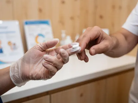 Close-up of a gloved hand applying cream to a finger against a clinical wooden background with visible product and clean lighting