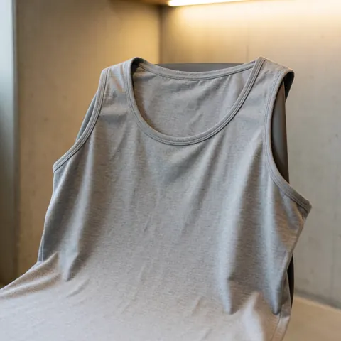 Gray cotton training t-shirt draped over a chair against a concrete wall with warm lighting highlighting the fabric texture