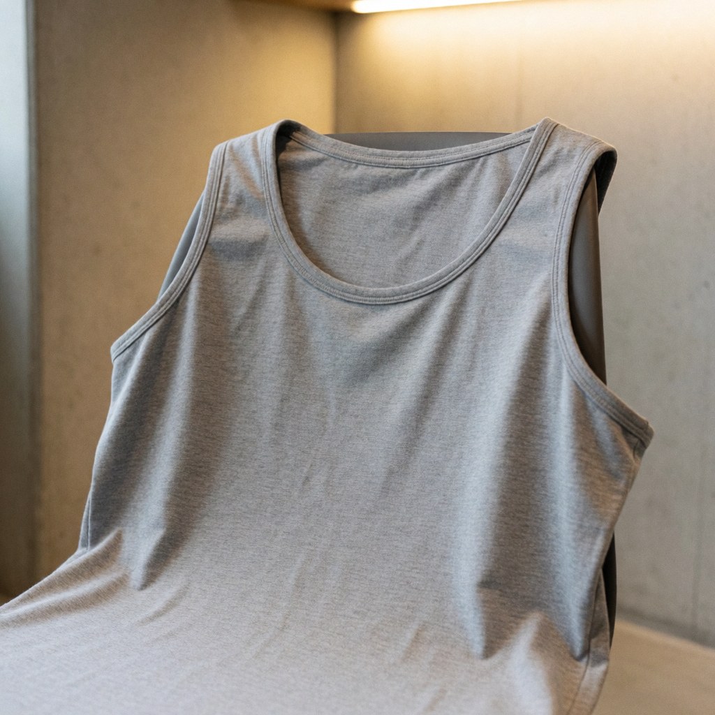 Gray cotton training t-shirt draped over a chair against a concrete wall with warm lighting highlighting the fabric texture