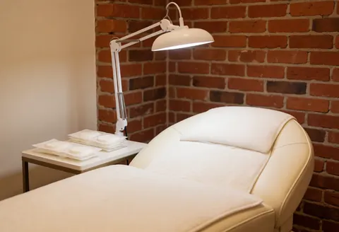 White treatment bed with adjustable lamp against red brick wall ready for service
