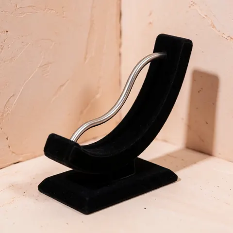 Curved titanium barbell piercing jewelry displayed on a black velvet stand against a light terracotta wall with soft studio lighting