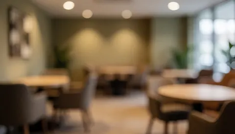 Blurred background of a meeting room with round tables, chairs, warm lighting, and earth-toned walls, ideal for community events.