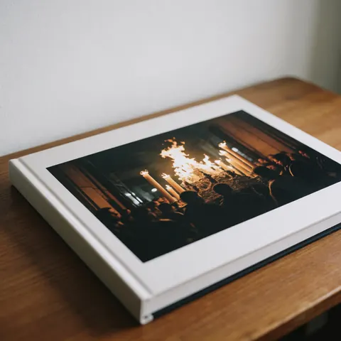 Open professional photobook on a wooden table showing a candlelight procession with dark attire under soft natural light