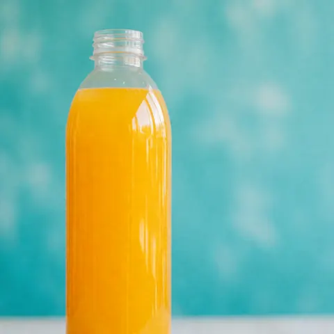 Transparent bottle filled with vibrant orange juice against a blurred turquoise backdrop, perfect for promoting refreshing beverages at water parks.
