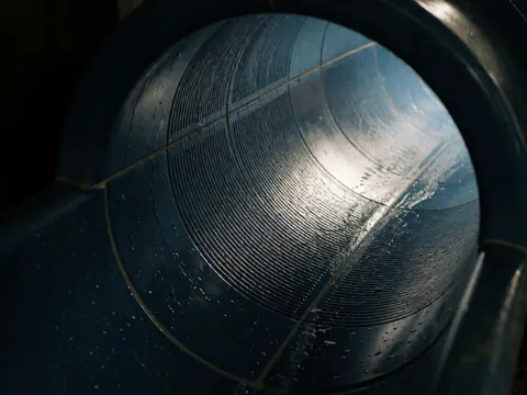 Close-up of the interior of a water slide tube showing flowing water, anti-slip texture, and artificial lighting against a dark background.