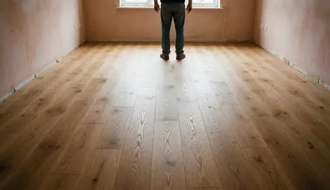 Installer inspecting newly installed hardwood floor in an empty room with plaster walls and natural light