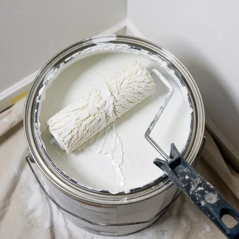 White paint roller submerged in an open bucket resting on protective drop cloth, ideal for plastering and finishing projects.