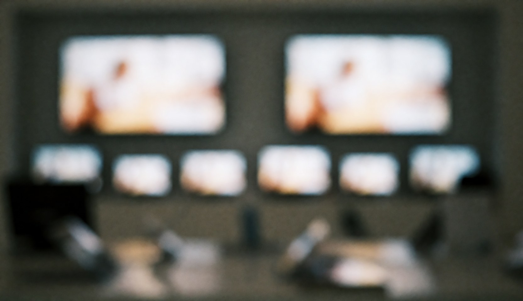 Out of focus background of multiple turned on tv screens in a room with warm and cool lights for advertising text