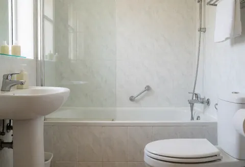 Clean modern private bathroom featuring a shower, sink, and toilet with light tiled walls suitable for lodging