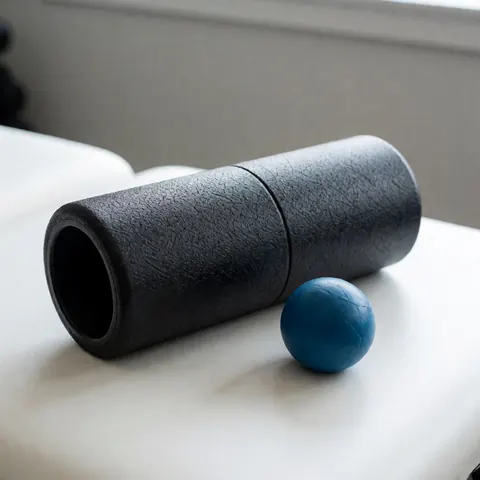 Black textured foam roller and blue lacrosse ball placed on a clean white table for sports massage therapy and physical training