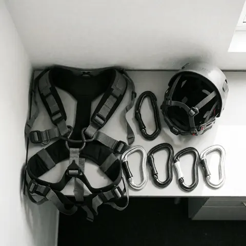 Professional climbing equipment including harness, helmet, and carabiners arranged on a clean white surface with natural lighting.