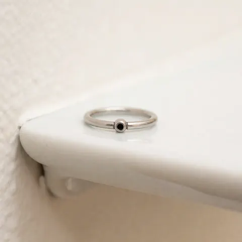 Close-up of a titanium ring with a black pearl displayed on a white plate against a warm neutral background