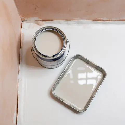 Synthetic paint can and tray with glossy paint on white cloth, light plaster walls, interior painting scene