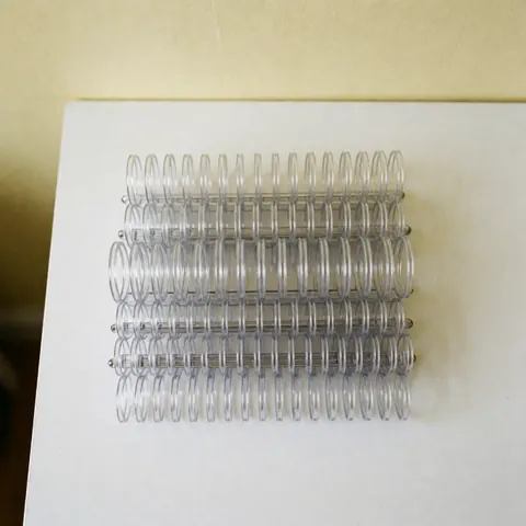 Rows of clear plastic binding combs stacked on a white table with a cream background, suitable for office and copy center supplies.